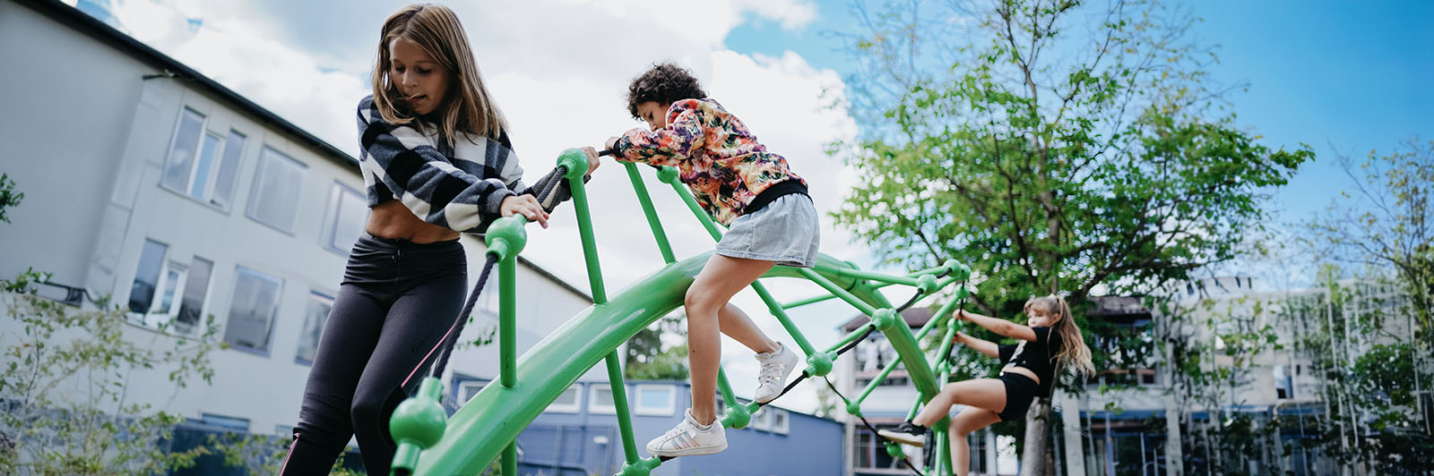 Children are focused on climbing across a winding steel climbing structure at a playground.